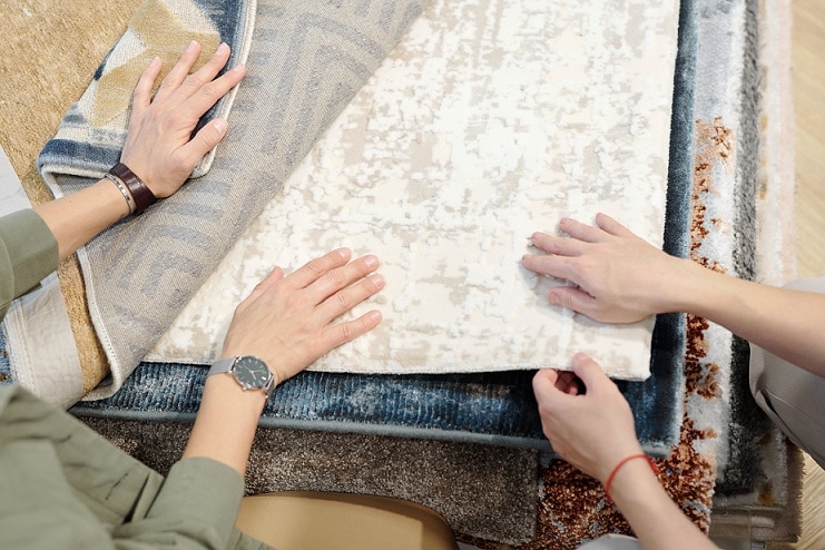 Hands of young female client and designer of contemporary studio of interior design touching sample of floor covering while choosing one